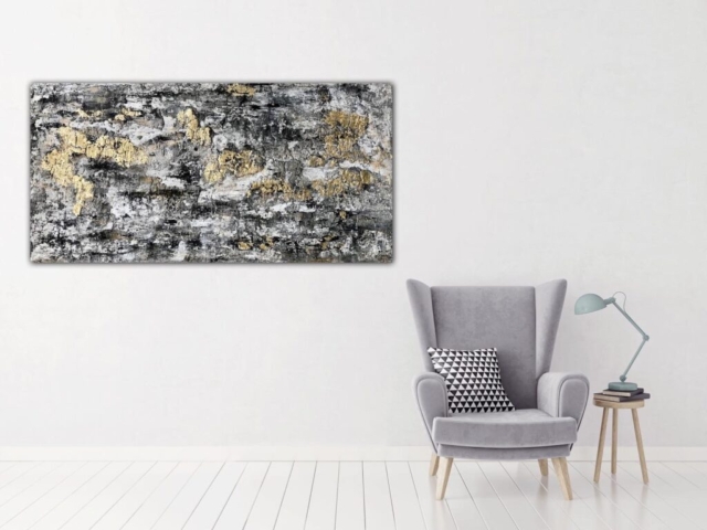 Großes abstraktes Bild in den Farben Schwarz und Grau mit Blattgold an einer Wand hängend. daneben ein Selssel.