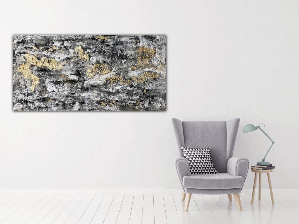 Großes abstraktes Bild in den Farben Schwarz und Grau mit Blattgold an einer Wand hängend. daneben ein Selssel.