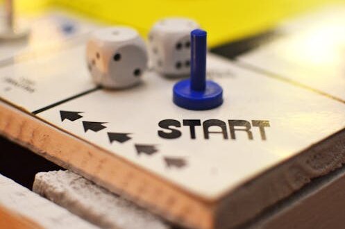 Auschnittvergrößerung des Startfeldes eines Spielbrettes. Darauf liegen zwei Würfel und eine Spielfigur. Alles steht auf Anfang. Haldewitzka Blog