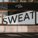 Ausschnittsfoto einer Hauswand. Im Fenster ist die Aufschrift "Sweet" zu sehen. Titelbild für den Beitrag Schweißgebadet in Bad Westernkotten.