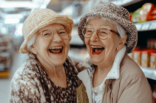 wei ältere Frauen mit Strohhüten und Brillen lachen herzlich in einem Supermarkt. Sie stehen eng beieinander vor einem Regal mit Lebensmitteln, strahlen Freude aus und wirken ausgelassen. Die Szene ist hell beleuchtet und vermittelt eine fröhliche Atmosphäre. Mein Wocheneinkauf: Denkanstöße inklusive