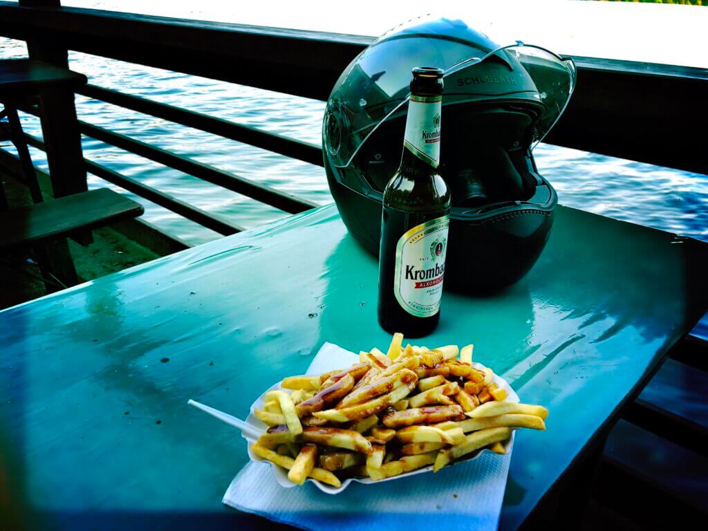 Motorradpause am See mit Schuberth-Helm, alkoholfreiem Krombacher Bier und Pommes mit Currysoße – entspanntes Biker-Erlebnis am Wasser