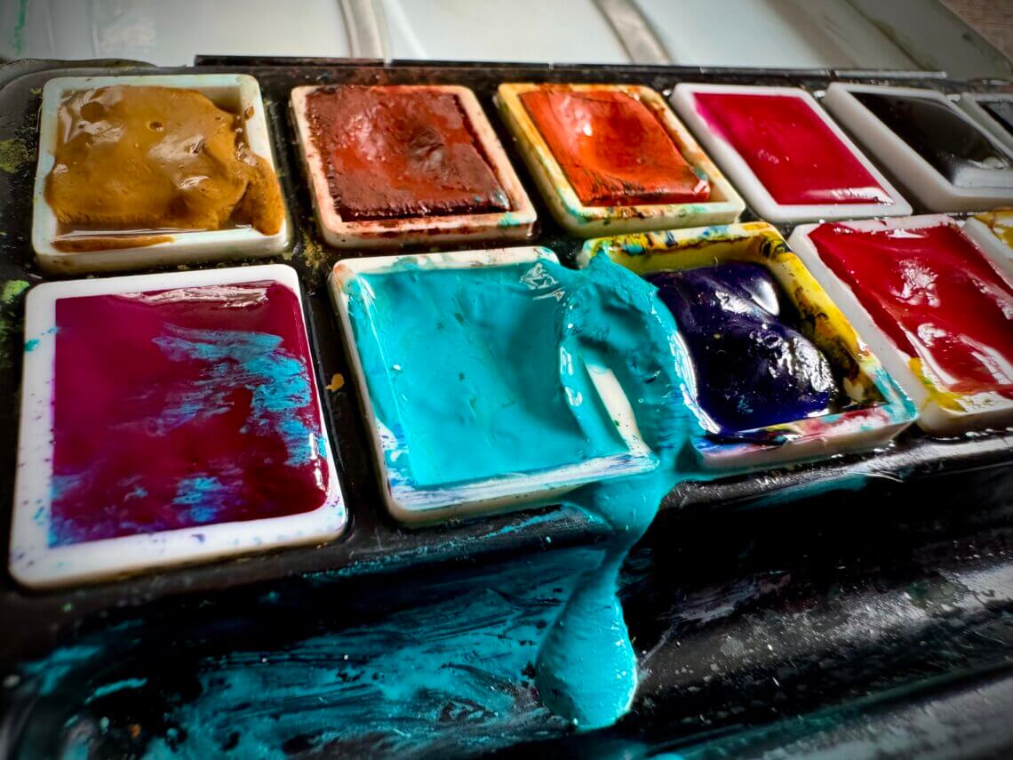 Kreativanfall - Nahaufnahme eines alten Aquarellkastens mit intensiven Farben – auslaufendes Türkis sorgt für kreative Unordnung – Symbol für künstlerische Inspiration, Malfreude und analoge Kreativität im Ruhestand.
