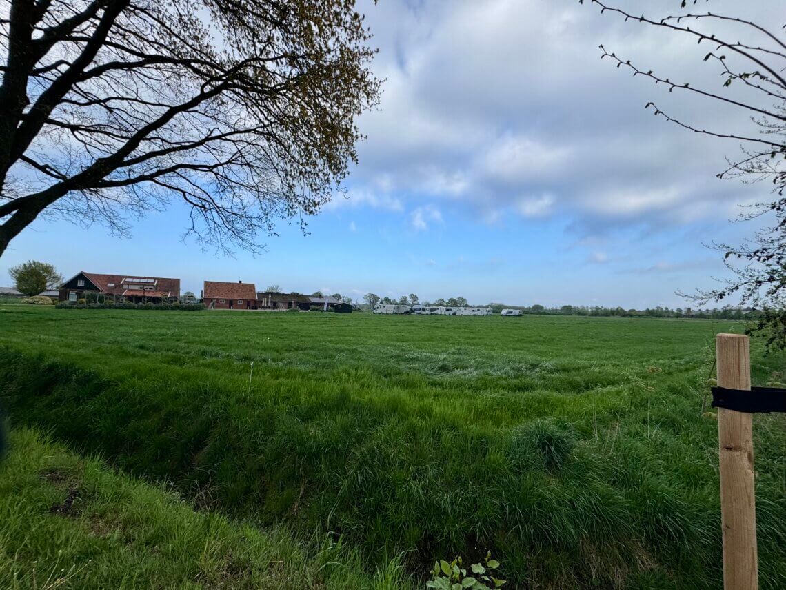 Wohnmobilstellplatz neben einem Bauernhof. Grüne Wiese drumherum mit blauem Himmel und ein paar Wolken.