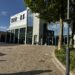 Moderne Glasfassade des Forum Velbert mit barrierefreiem Eingangsbereich, umliegenden Bäumen und großzügigem gepflasterten Vorplatz bei sonnigem Wetter; im Hintergrund ein Netto-Supermarkt. Poetry Slam Velbert