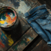 Ein Jeans auf einer mit Farbe beschmierten Werkbank. Daneben ein Topf mit Farbe in verschiedenen Tönen. Drabble am Dienstag.