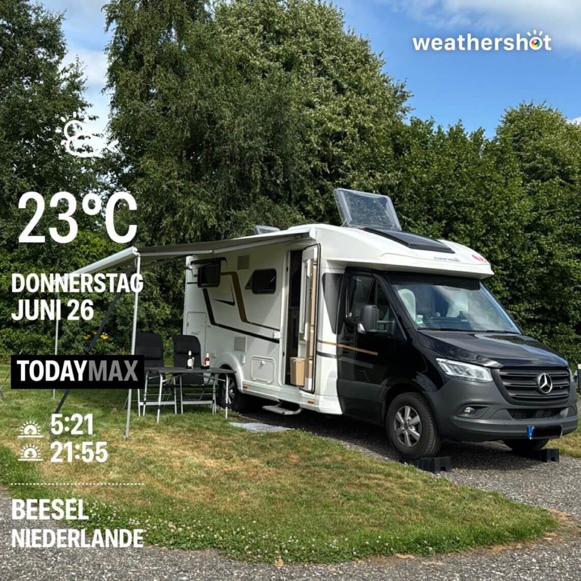 Modernes Wohnmobil auf einem Campingplatz in Beesel, Niederlande, bei sonnigem Wetter am 26. Juni. Temperatur 23 °C, Sonnenaufgang um 5:21 Uhr, Sonnenuntergang um 21:55 Uhr. Der Mercedes-Camper steht auf einer Parzelle mit Markise, Campingstühlen und Tisch, umgeben von grünen Bäumen.“