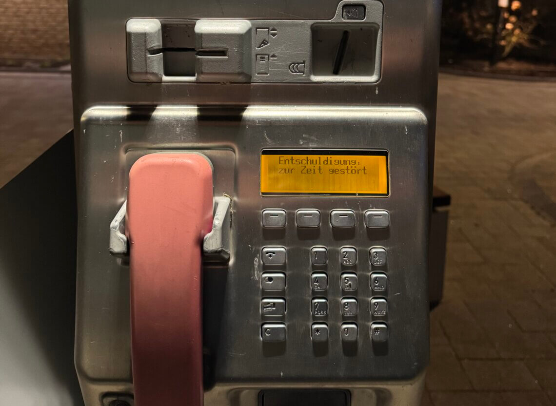 Nahaufnahme eines defekten öffentlichen Telekom-Telefons mit rosa Hörer und gelber Displayanzeige mit der Meldung ‚Entschuldigung, zur Zeit gestört‘, Erinnerungen Telefonzellen Telefonzellen Nostalgie Kommunikationskultur