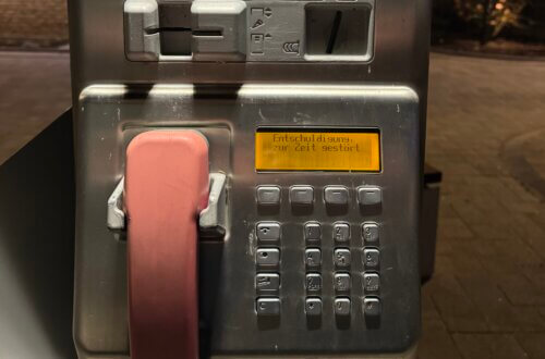 Nahaufnahme eines defekten öffentlichen Telekom-Telefons mit rosa Hörer und gelber Displayanzeige mit der Meldung ‚Entschuldigung, zur Zeit gestört‘, Erinnerungen Telefonzellen Telefonzellen Nostalgie Kommunikationskultur