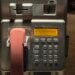 Nahaufnahme eines defekten öffentlichen Telekom-Telefons mit rosa Hörer und gelber Displayanzeige mit der Meldung ‚Entschuldigung, zur Zeit gestört‘, Erinnerungen Telefonzellen Telefonzellen Nostalgie Kommunikationskultur