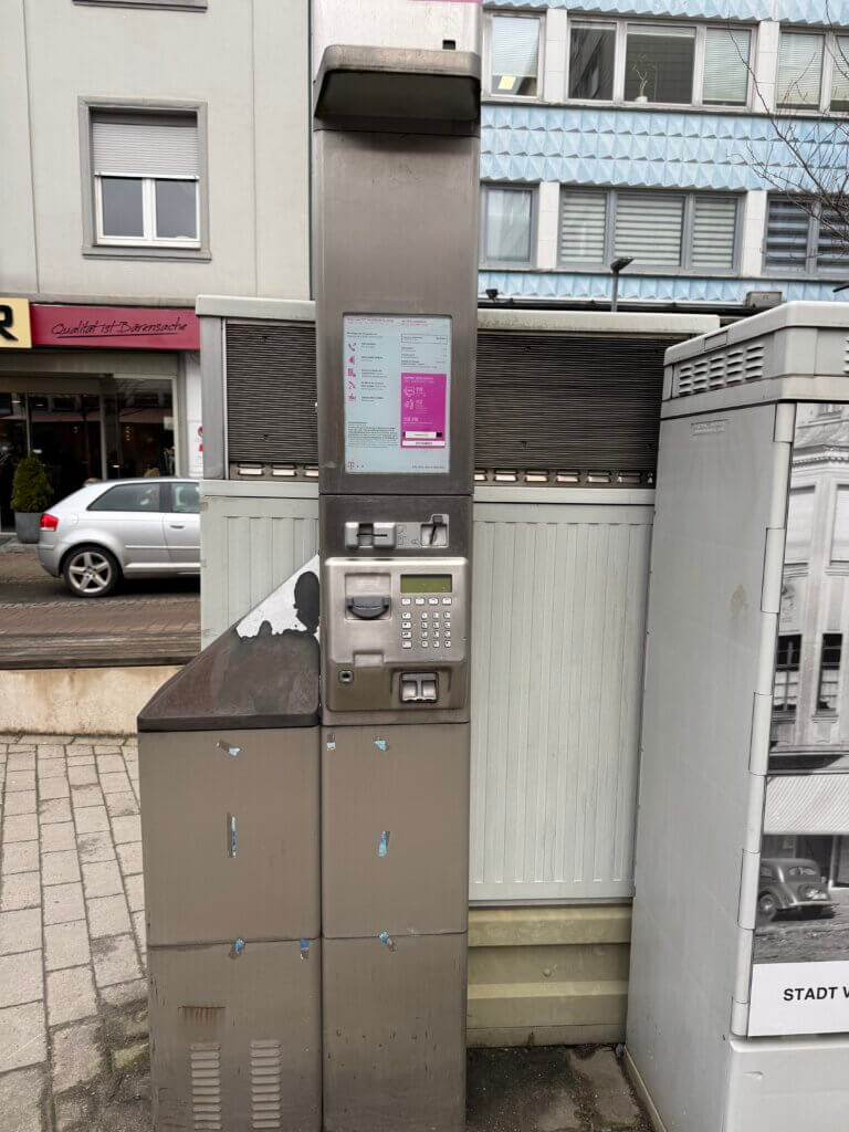 Altes öffentliches Telekom-Telefon in Edelstahl-Ausführung mit Tastenfeld und Kartenschlitz, stehend auf einem Gehweg in einer deutschen Innenstadt Telefonzellen Nostalgie Kommunikationskultur