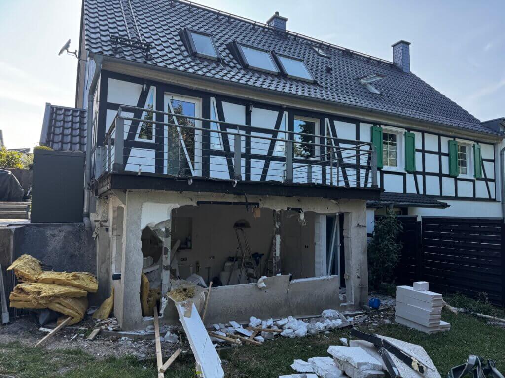 Halbfertiger Abriss eines Anbaus an einem Fachwerkhaus mit sichtbaren Baumaterialien und Bauschutt im Garten – Umbau- oder Renovierungsarbeiten im privaten Wohnhaus. Halbzeit im Ruhestand 2025