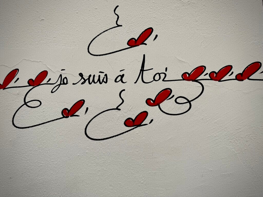 Wandinschrift in französischer Schreibschrift mit roten Herz-Elementen und dem Text „je suis à toi“ Streettypografie