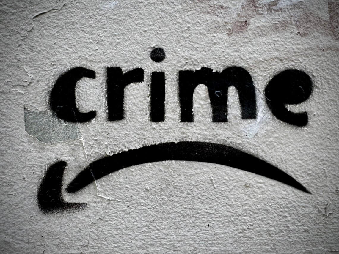 Schablonengraffiti mit dem Wort “crime” und geschwungenem Pfeil auf rauer Hauswand. Streettypografie