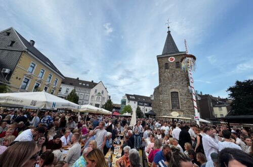 Weinfest in Velbert mit Menschenmengen vor Kirchturm bei Sonnenschein.