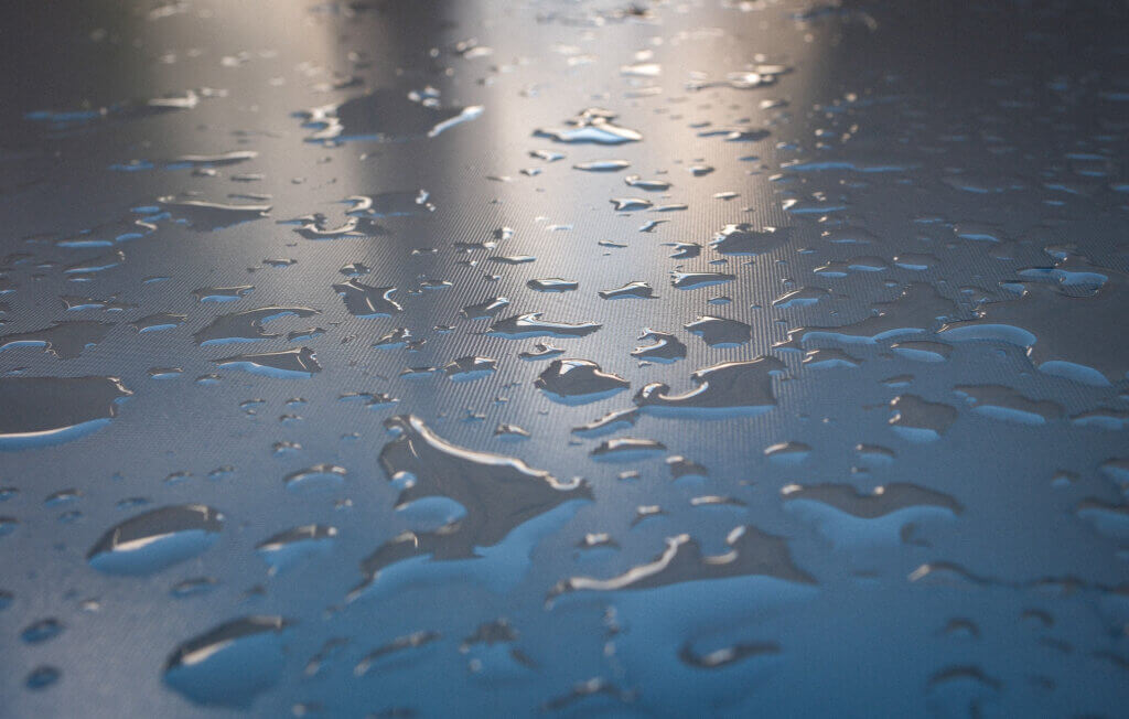 Nahaufnahme von Wassertropfen auf einer strukturierten, dunkelgrauen Oberfläche bei weichem Licht – Wassertropfen spiegeln die Umgebung und erzeugen ein natürliches Muster. Projekt52: Regen