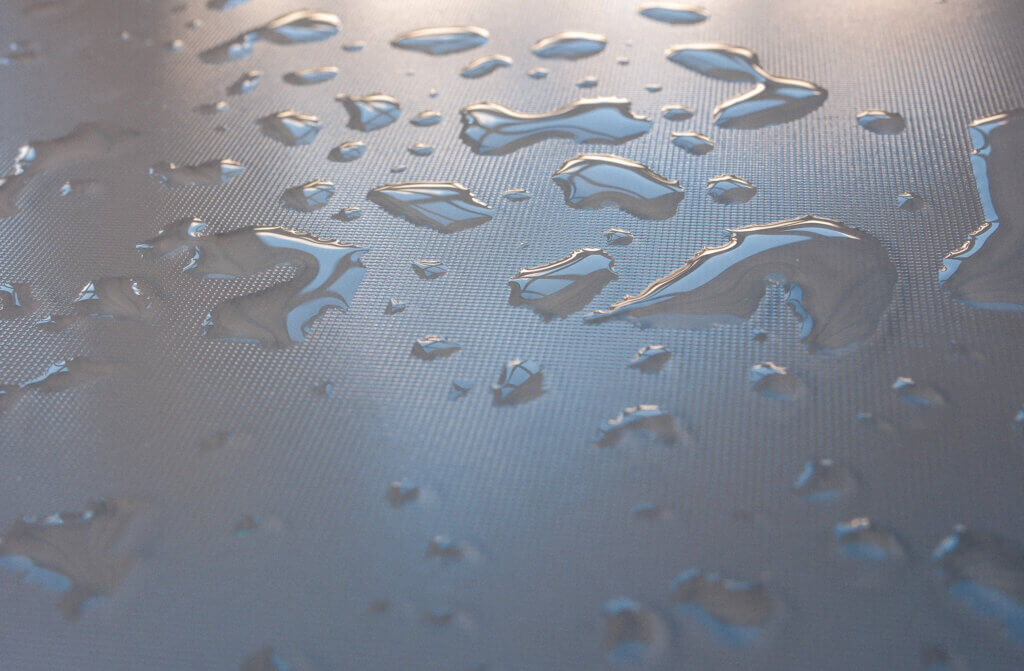 Detailansicht von klaren Wassertropfen auf einer strukturierten Oberfläche mit reflektierendem Licht – geometrisches Muster im Hintergrund sichtbar. Projelt52: Regen