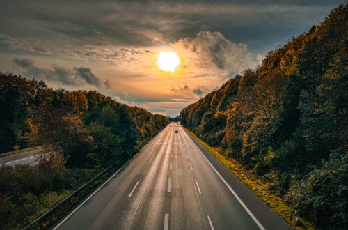 Leere Autobahn im Licht der untergehenden Sonne, umgeben von bunt gefärbtem Herbstwald – stimmungsvolles Foto einer herbstlichen Reise in den Ruhestand.