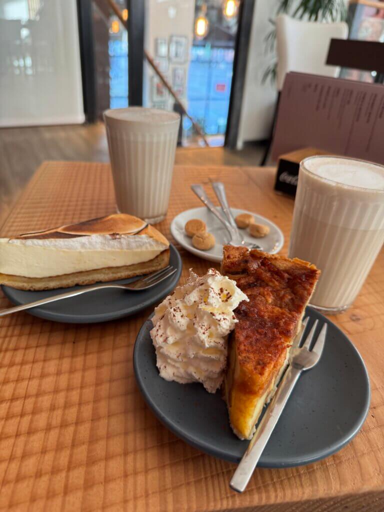 Zwei Gläser Milchkaffee, ein Stück Käsekuchen und ein Stück herzhafte Quiche mit Sahne auf einem Holztisch in einem gemütlichen Café in Sneek.