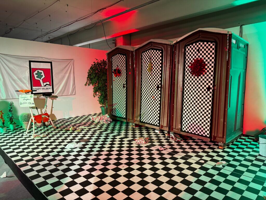 Theaterbühne in der Küchenabteilung eines Möbelhauses in Velbert mit Schachbrettmuster-Boden, roter und grüner Bühnenbeleuchtung und Holzkulisse für die Aufführung zum 50-jährigen Jubiläum der Gebietsreform. Monatsrückblick November 2025