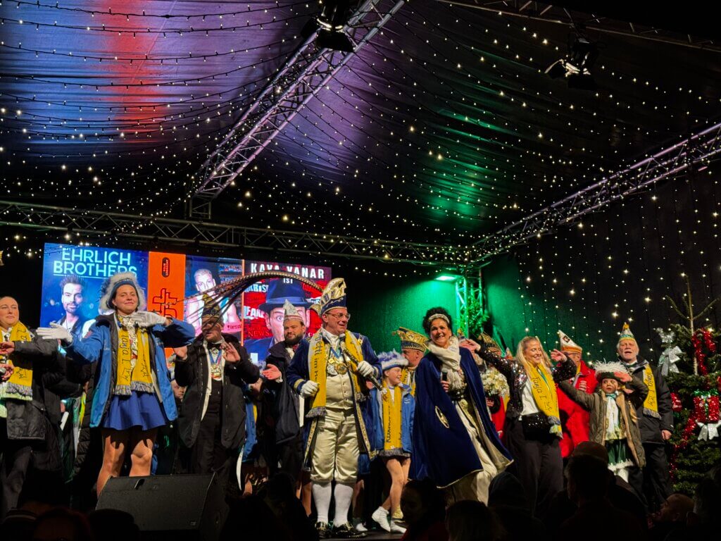 Karnevalstruppe auf der Bühne des Weihnachtsmarkts Essen-Steele mit bunter Lichterketten-Dekoration und festlichen Kostümen, Eröffnungsveranstaltung November 2025