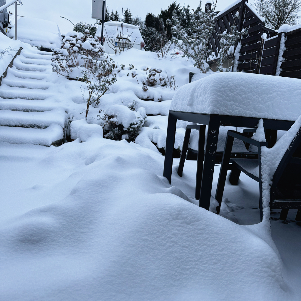 Tief verschneiter Garten mit eingeschneiten Gartenmöbeln und Treppe, Wintereinbruch Januar 2025