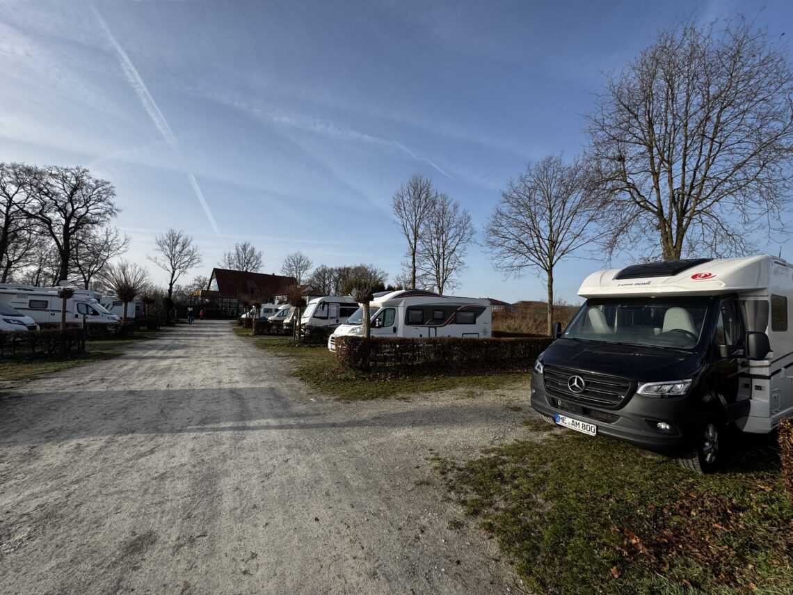 Campingplatz Rumkerhof. Fahrweg mit Wohnmobilen rechts und link. Blick auf das Hauptgebäude im Hintergrund