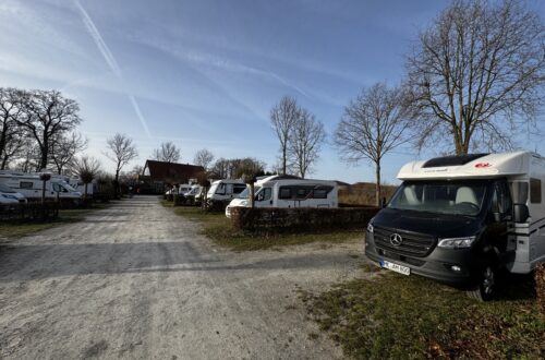 Campingplatz Rumkerhof. Fahrweg mit Wohnmobilen rechts und link. Blick auf das Hauptgebäude im Hintergrund