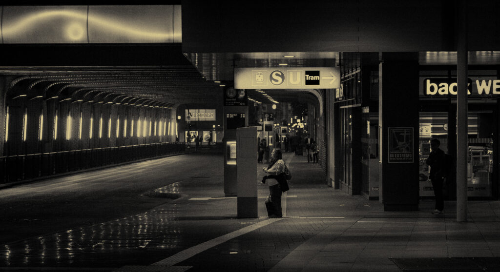 Einsame Frau wartet nachts an einem Bahnsteig am Essen Hauptbahnhof, Schwarz-Weiß mit warmem Gegenlicht, Straßenfotografie Ruhrgebiet
