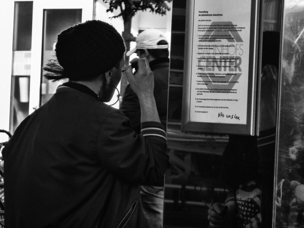 Junger Mann schminkt sich vor dem Aushangschild des BahnhofsCenters Gelsenkirchen, Schwarz-Weiß-Streetfotografie