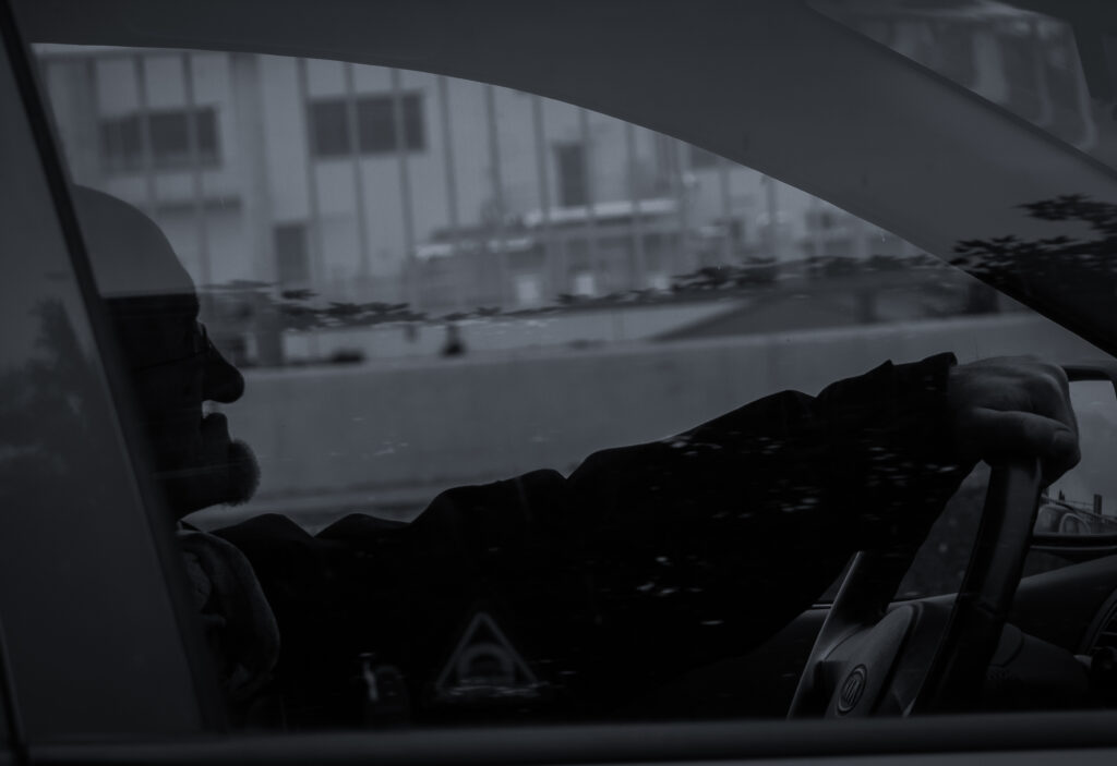 Silhouette eines älteren Mannes am Steuer, durch das Seitenfenster fotografiert, Schwarz-Weiß-Streetfotografie im urbanen Raum