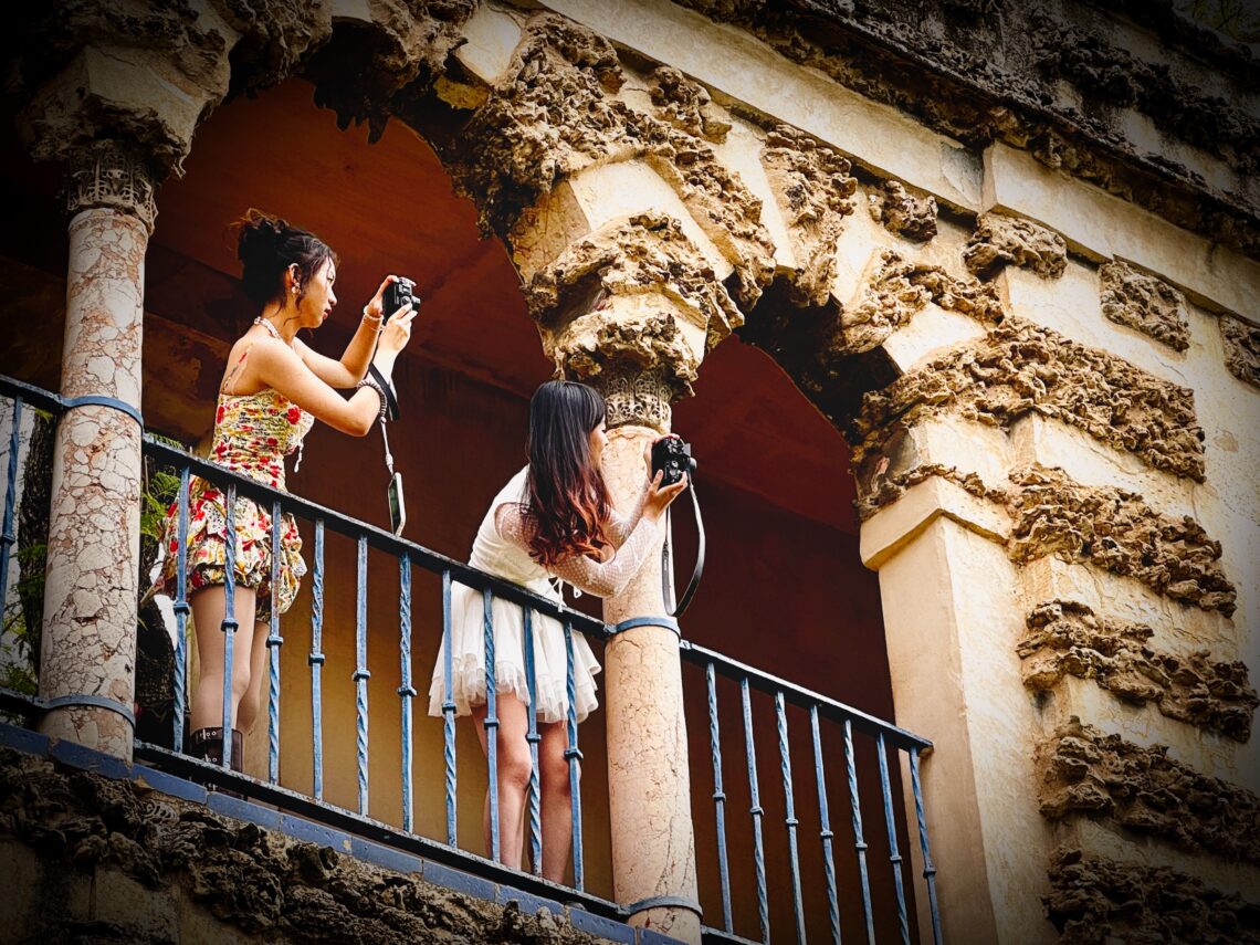 Zwei Frauen fotografieren von einem Balkon mit verzierter Fassade – Streetfotografie in warmen Farben und architektonischen Details