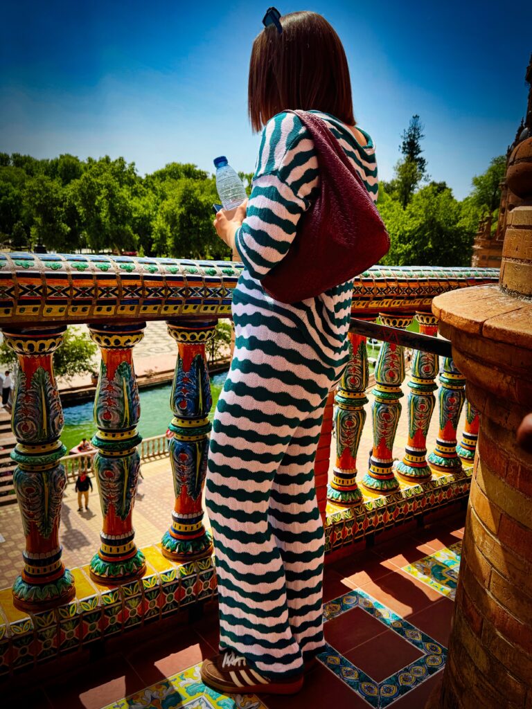 Frau mit gestreiftem Kleid und roter Tasche auf bunter Brücke in Sevilla – farbenfrohe Streetfotografie mit urbanem Flair