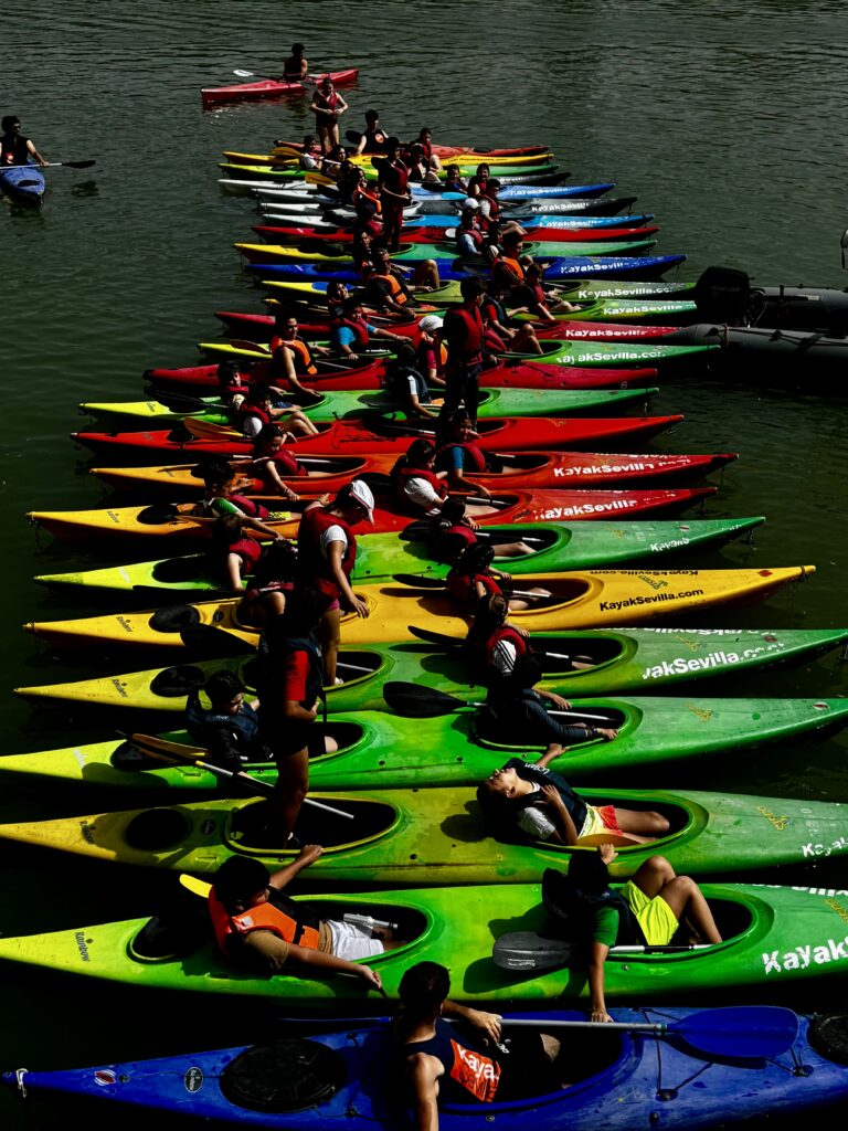 Bunte Kajaks mit Menschen auf einem Fluss in Sevilla – lebendige Streetfotografie mit starken Farben und Mustern