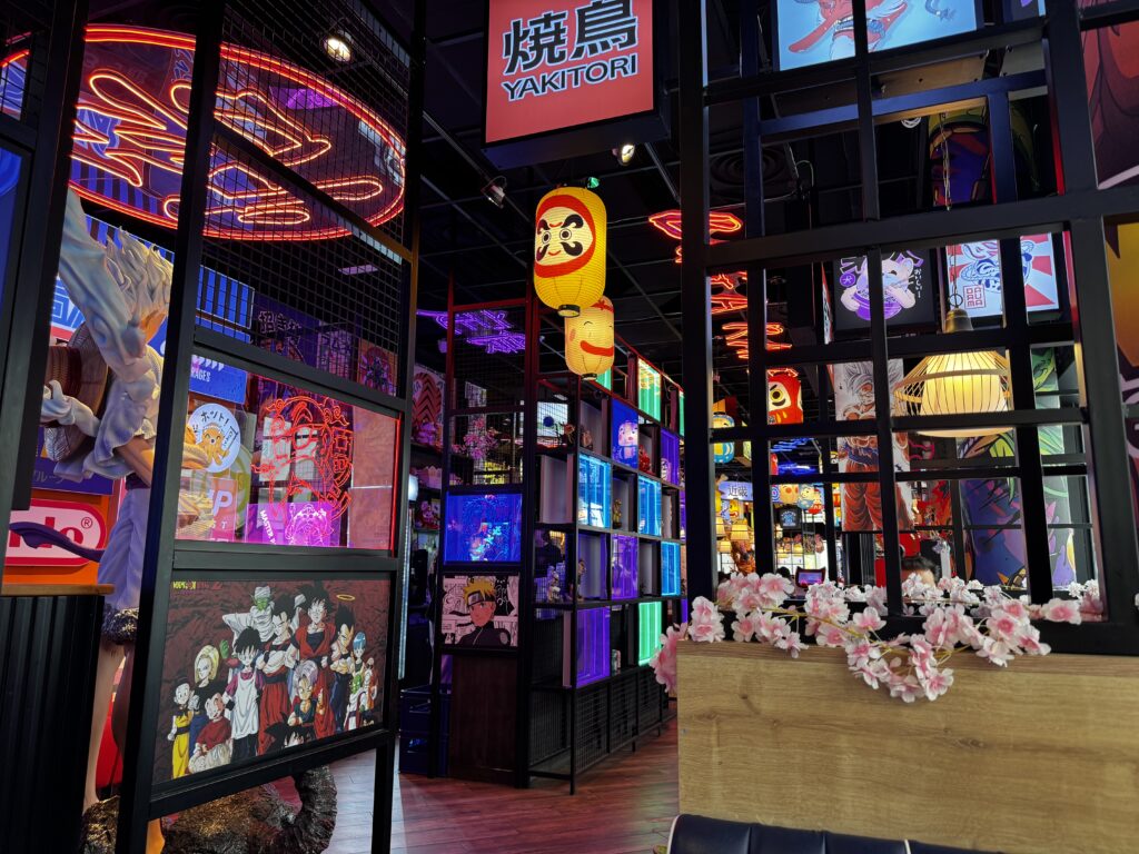 Buntes Interieur eines Yakitori-Restaurants mit Neonlichtern, Anime-Kunstdrucken, Daruma-Laternen und japanischen Dekorationselementen in mehrgeschossigen Regalen