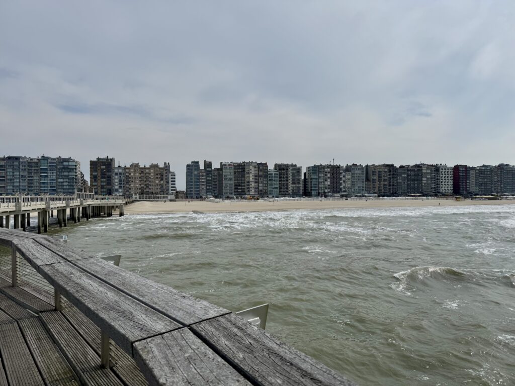 Blick von der Seebrücke in Blankenberge auf Strand, Nordsee und die dichte Hochhausfront an der belgischen Küste.