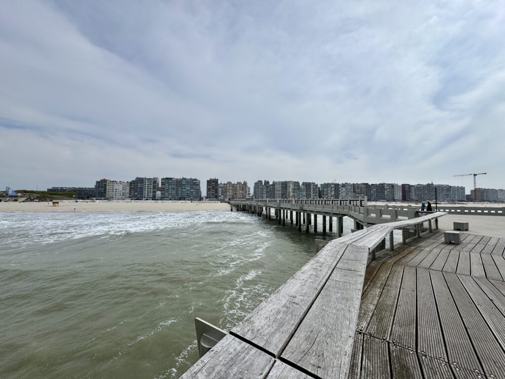 Blick von der Seebrücke in Blankenberge auf Strand, Nordsee und die dichte Hochhausfront an der belgischen Küste.