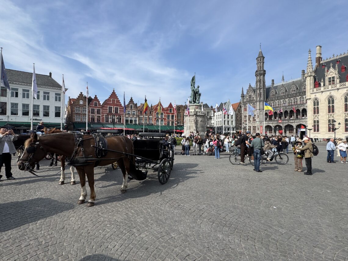 Marktplatz von Brügge mit historischen Fassaden, Pferdekutsche und Besuchern in der Altstadt.
