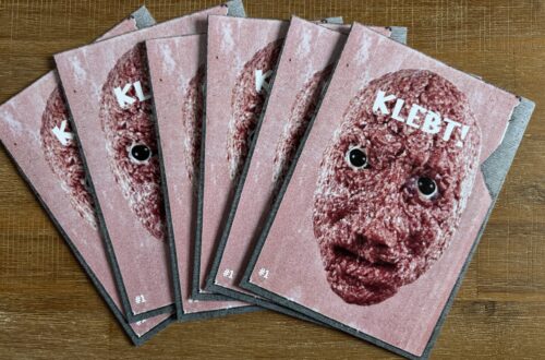 Stapel des gedruckten Fotozines KLEBT! Ausgabe 1 mit dem Titelmotiv eines Mettgesichts mit Kulleraugen auf rosafarbenem Hintergrund.