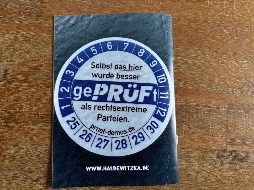 Rückseite des Fotozines mit einem runden Sticker im Stil einer Prüfplakette mit der Aufschrift „gePRÜFt - Selbst das hier wurde besser als rechtsextreme Parteien“ und dem Schriftzug haldewitzka.de am unteren Bildrand.