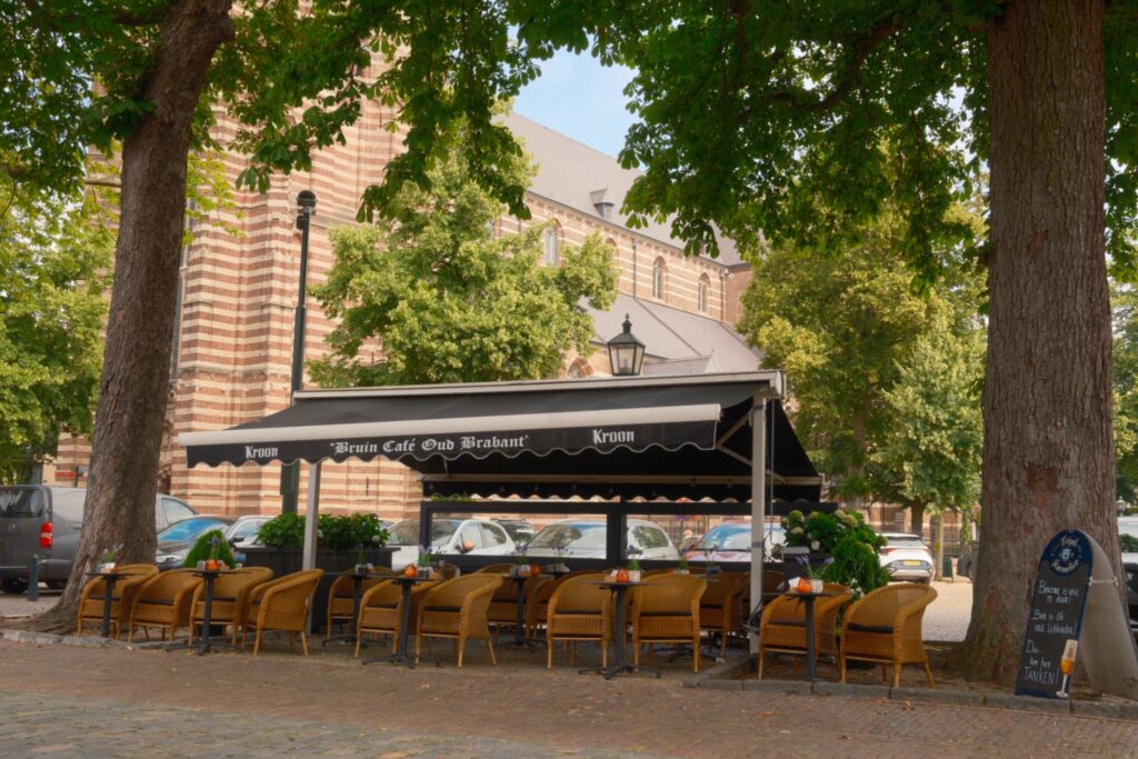 Gemütlicher Gastronomie-Außenbereich des Bruin Café Oud Brabant am Marktplatz in Oirschot mit Blick auf die Kirche.