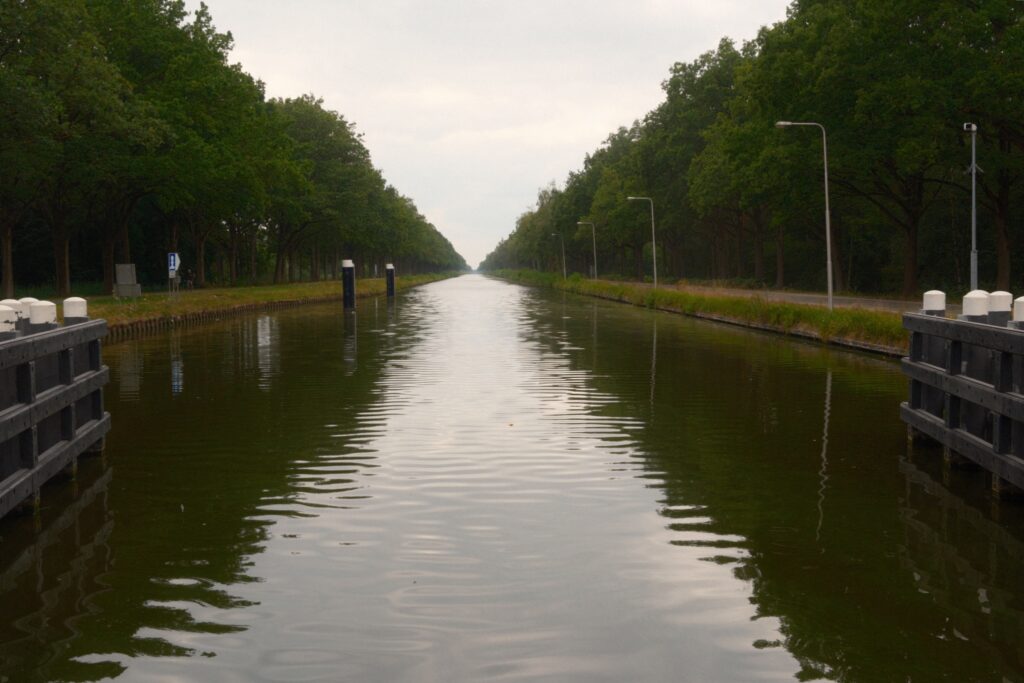 Schnurgerader Wilhelminakanal mit baumbestandenen Ufern und flachem Wasser unter bedecktem Himmel.