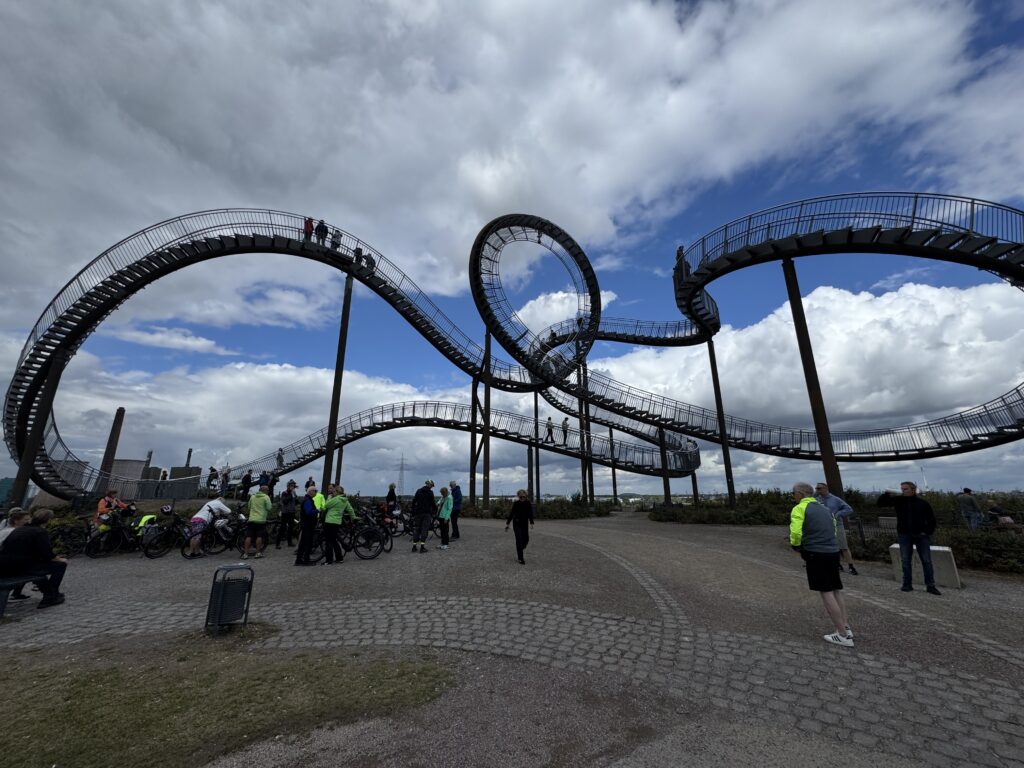 Skulptur Tiger and Turtle in Duisburg mit begehbarer Achterbahn-Treppe vor bewölktem Himmel, Radfahrer im Vordergrund