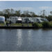 Aufnahme vom Wasser aus auf eine Reihe geparkter Wohnmobile am Ufer des Camperplaats aan de Ee bei Dokkum.