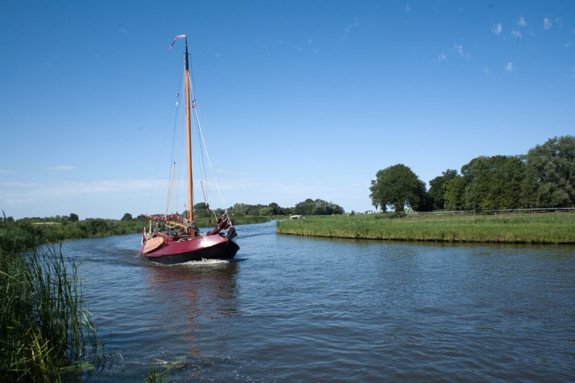 Traditionelles rotes Segelboot auf einem ruhigen Kanal in Friesland, umgeben von Wiesen und Bäumen