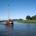Traditionelles rotes Segelboot auf einem ruhigen Kanal in Friesland, umgeben von Wiesen und Bäumen