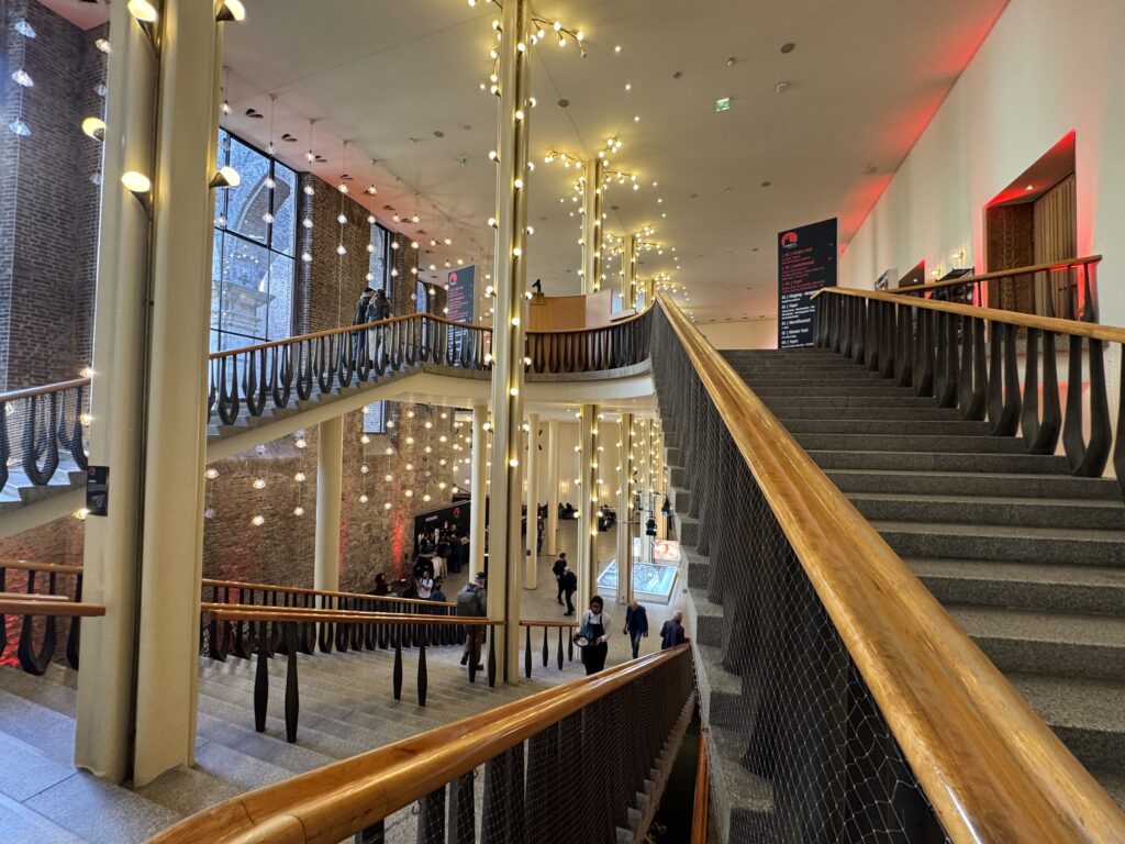 Architektur des Gürzenich-Foyers in Köln mit Blick auf die geschwungene Treppe, Hängelampen und große Fenster.