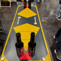 Geschicklichkeitsspiel mit Bierflaschen auf gelb-schwarzem Spieltisch – humorvoller Turnierstand auf der SPIEL Essen.