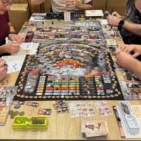 Intensives Spielen am voll belegten Spieltisch – detailreiches Brettspiel mit Würfeln, Ressourcen und Spielkarten auf der SPIEL Essen.