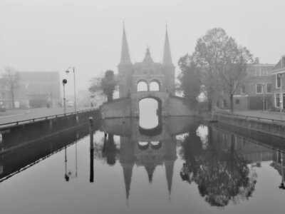 Historisches Wassertor in Sneek mit zwei Türmen spiegelt sich im ruhigen Wasser eines Kanals bei dichtem Nebel.